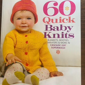 May include: A softcover book titled 60 Quick Baby Knits featuring a child wearing a pink and orange knit hat and a yellow knit cardigan with red buttons. The cover text lists blankets, booties, sweaters and more in Cascade 220 Superwash.