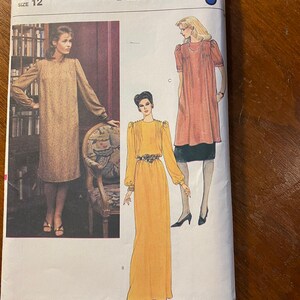 以下が含まれることがあります： ヴォーグパターン製のドレスの裁縫パターン、サイズ12。パターンは、ギャザーネックの半袖ドレス、ギャザーネックの長袖ドレス、ギャザーネックとベルト付きの長袖ドレスの3つの異なるスタイルのドレスを示しています。