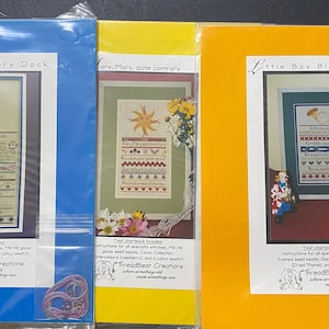 Puede incluir: Tres patrones de punto de cruz en cartulina amarilla, azul y naranja. Los patrones se titulan "Hickory Dickory Dock", "Mary, Mary, Quite Contrary" y "Little Boy Blue". Cada patrón incluye instrucciones para puntadas especiales, cuentas de semillas y una muestra de calicó.