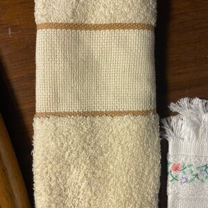May include: A white hand towel with a brown trim. The towel is folded and has a soft, fluffy texture.