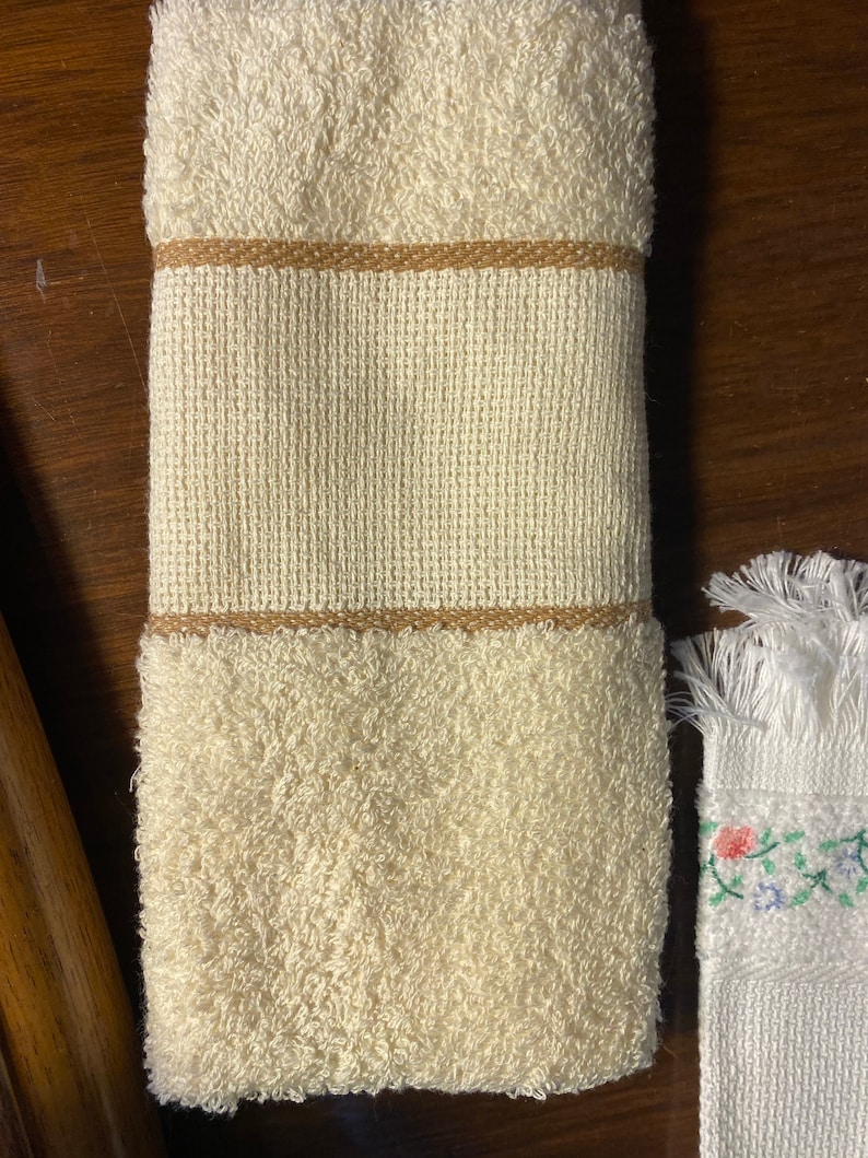 May include: A white hand towel with a brown trim. The towel is folded and has a soft, fluffy texture.