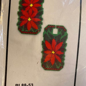 May include: A set of two red poinsettia door knob covers. The covers are made of fabric and have a green background. The text on the packaging reads "PL88-53 Poinsettia Set of Two Doorknob Covers".