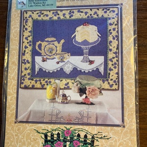 May include: A quilting pattern for a quilt titled "Lemon Drops & China Blue" designed by Elle Colquitt. The pattern features a teapot, teacup, cake, and flowers. The pattern is framed by a picket fence with flowers.