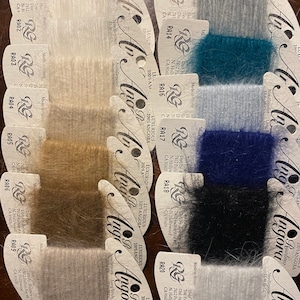 Puede incluir: Una colección de 10 ovillos de hilo de angora lujoso en varios colores, incluyendo blanco, gris, azul verdoso, azul y marrón. Cada ovillo está etiquetado con el nombre de la marca "Angora" y el número de color. El hilo es suave y esponjoso, y es perfecto para tejer o hacer ganchillo.