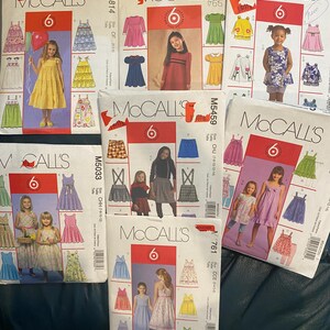 May include: A collection of six McCall's sewing patterns for children's clothing. The patterns are for sizes 7-14 and feature a variety of styles, including dresses, skirts, and tops. The patterns are printed on white paper with colorful illustrations.