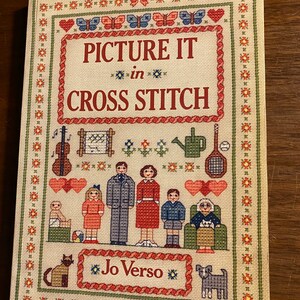 May include: A book cover with a cross stitch design featuring a family, a cat, a dog, and the text "Picture It in Cross Stitch" by Jo Verso.