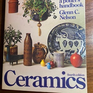 May include: A book cover titled "Ceramics" with the text "a potter's handbook" and the author's name, Glenn C. Nelson. The cover features various ceramic objects, including a hanging planter, a plate, and several vases.