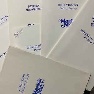 May include: A collection of vintage sewing patterns with white covers and blue text. Titles include "Dogwood," "Hollyhocks," and "Morning Glory." The "Mountain Mist" logo is visible on several patterns. Some patterns have handwritten signatures.