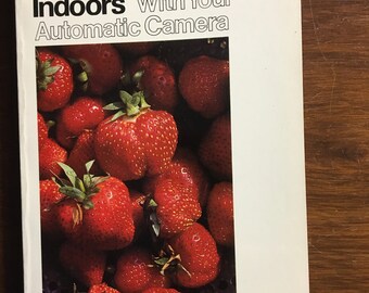 Pode incluir: Uma capa de livro com o título "Fotografar em ambientes fechados com sua câmera automática" em negrito preto. A capa apresenta uma imagem em close-up de uma tigela de morangos vermelhos.