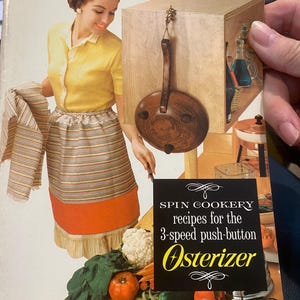 May include: A vintage advertisement for the Osterizer 3-speed push-button blender. The ad features a woman in a yellow blouse and striped skirt standing in a kitchen. The Osterizer blender is shown in the foreground with a bowl of vegetables and a cauliflower.