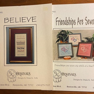 Puede incluir: Dos diseños de papel impresos para proyectos de punto de cruz. Uno presenta la palabra "BELIEVE" con un diseño enmarcado. El otro muestra corazones bordados enmarcados con el texto "Friendships Are Sewn".