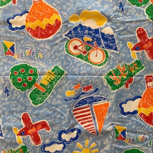 May include: Pale blue fabric featuring a repeating pattern of vibrant illustrations. The design includes hot air balloons, airplanes, bicycles, kites, sailboats, suns, clouds, trees, and fish. The illustrations are in red, orange, yellow, green, and blue.