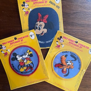 Op de afbeelding: Drie strijkbare patches met Disney-figuren. De patches zijn op gele kaarten met rode randen. De eerste patch is blauw met een rode strik en toont Mickey Mouse. De tweede patch is rood met een witte rand en toont Mickey en Minnie Mouse. De derde patch is blauw met een gele rand en toont Pluto.