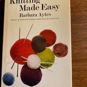 May include: A book cover titled "Knitting Made Easy" by Barbara Aytes. The cover features colorful yarn balls in red, brown, green, white, and purple, with knitting needles. The text "Achieve professional-looking results from the beginning" is also visible.