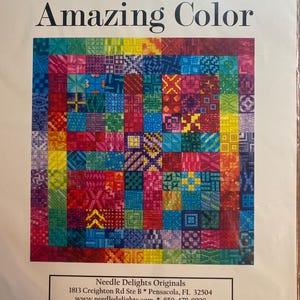 May include: A colorful needlepoint pattern titled "Amazing Color." The design features a patchwork of small squares in various colors, including red, blue, green, and yellow. The text "Needle Delights Originals" is at the bottom.