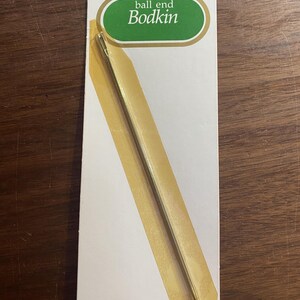 May include: A J. & P. Coats N. 463 ball end bodkin sewing tool packaged on a white card. The metal bodkin features a long, slender shaft with a rounded ball tip at one end and a slotted eye at the other. The packaging includes green and white text.