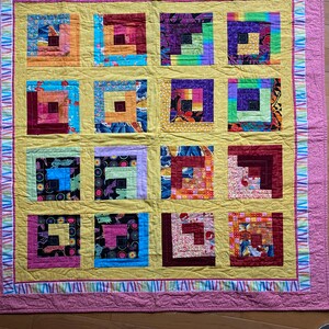 Puede incluir: Una colcha amarilla con un borde rosa y un patrón de cuadrados coloridos. Los cuadrados están hechos de diferentes telas y tienen un diseño de cabaña de troncos.