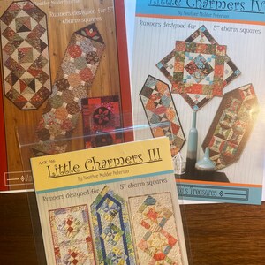 May include: Three quilting pattern books titled "Little Charmers", "Little Charmers III", and "Little Charmers IV". Each book features a colorful quilt runner design made with 5-inch charm squares.