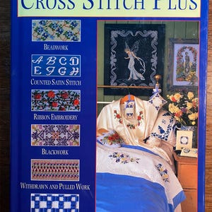 Pode incluir: Um livro intitulado "Cross Stitch Plus" com uma capa azul e uma variedade de desenhos de ponto cruz na capa. Os desenhos incluem bordado com miçangas, ponto de cetim contado, bordado com fita, bordado preto, trabalho retirado e puxado, e hardanger.