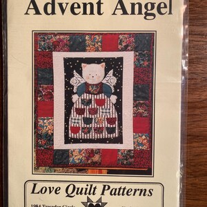 Peut inclure: Un modèle de courtepointe murale représentant un ange avec un visage de chat blanc et des ailes. L'ange porte une robe à rayures rouges et blanches et tient un cœur. Le modèle est intitulé "Advent Angel" et provient de Love Quilt Patterns.