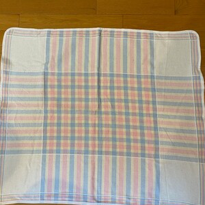 May include: A white checkered blanket with pink, blue, and yellow stripes. The blanket has a white border.