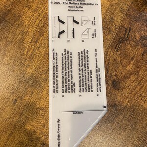 Könnte beinhalten: Ein weißes Kunststoff-Quilting-Werkzeug mit Anweisungen und Diagrammen. Das Werkzeug ist mit "The Binding Tool" beschriftet und enthält Text zum Nähen von Bindungen. Es dient zum präzisen Schneiden und Nähen für Quiltprojekte.