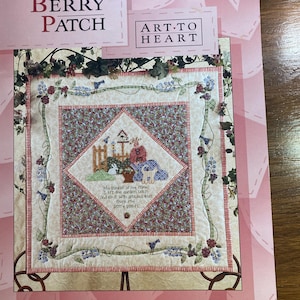 Puede incluir: Un patrón de colcha rosa y blanco con un diseño floral y el texto "In My Berry Patch" y "Art-To-Heart". El patrón de colcha presenta una casita para pájaros, una cerca y una cesta de bayas.