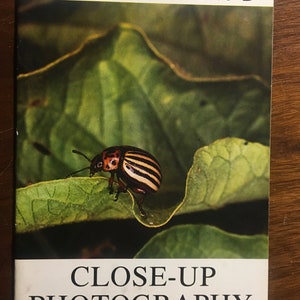 Op de afbeelding: Een boek getiteld "CLOSE-UP PHOTOGRAPHY" met een Hasselblad-logo op de omslag. De omslag toont een close-up van een zwart-geel gestreepte kever op een groen blad.
