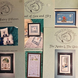 May include: A collection of cross stitch patterns featuring a variety of designs, including a fairy pillow, a sentinel of sea and sky, a maiden and a unicorn, and a castle with a poem. The patterns are from Dragon Dreams, a cross stitch design company.