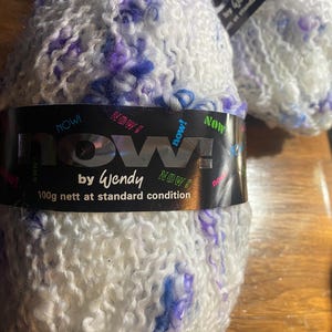 May include: White yarn with blue and purple flecks. The label reads "now! by Wendy" and "100g nett at standard condition". The yarn has a textured, looped appearance, suitable for knitting or crochet projects.