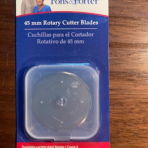 May include: Package of three 45 mm rotary cutter blades for fabric cutting. The blades are made of tungsten-carbon steel. The package is blue and white with the Fons & Porter logo. The text on the package reads "45 mm Rotary Cutter Blades" and "Cuchillas para el Cortador Rotativo de 45 mm".