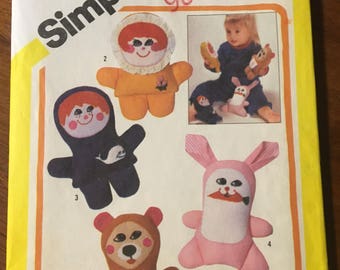 Puede incluir: Un patrón de costura Simplicity vintage con diseños de animales de peluche, incluyendo un oso, un conejo y una muñeca. El patrón incluye el texto "ONE SIZE" y "PLAYSKOOL". El patrón tiene un esquema de color amarillo y blanco.