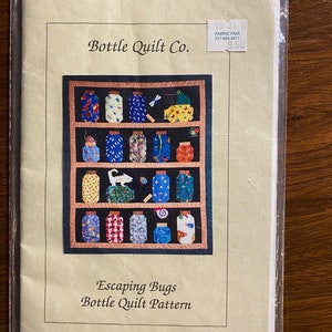 May include: A Bottle Quilt Co. sewing pattern titled Escaping Bugs Bottle Quilt Pattern. The cover features a quilt design with rows of colorful jars containing various insects and small creatures on a dark background with peach borders.