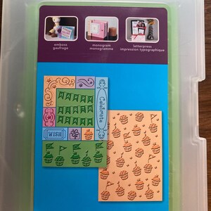 Op de afbeelding: Een doorzichtige plastic opbergdoos met een knutselvel op een blauwe achtergrond. Het vel bevat diverse rubberen stempels, waaronder cupcake-patronen, een "HAPPY BIRTHDAY"-banner en het woord "Celebrate" in een verticale oriëntatie.
