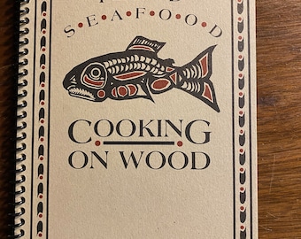 May include: A brown cookbook with a spiral binding. The cover features a stylized salmon illustration and the text "PLANKED S•E•A•F•O•O•D COOKING ON WOOD".