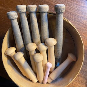 May include: A bowl filled with wooden knitting needles of various sizes and colors. The needles are mostly natural wood color, with a few painted pink.
