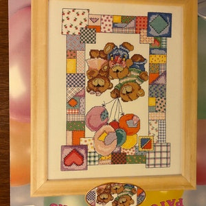 May include: Cross stitch pattern featuring a patchwork design with three teddy bears holding balloons. The pattern is framed in a light wood frame. The text on the pattern reads "Patchwork Bears".