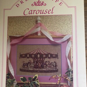 May include: A cross-stitch pattern leaflet titled Dreamscape Carousel, featuring a framed embroidery of a carousel with horses. The cover displays the text Leaflet 7, Dreamscape Carousel, and Designed by Teresa Wentzler, with pink and white ribbons.