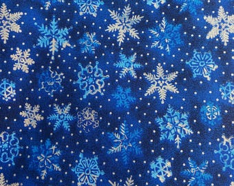 May include: A fabric with a dark blue background, covered in various snowflake designs in shades of blue and silver. Small white dots are scattered throughout the pattern, creating a wintery theme. The snowflakes vary in size and detail.