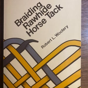 May include: A book titled "Braiding Rawhide Horse Tack" by Robert L. Woolery. The cover features a woven design in yellow, gray, and blue on a cream background. The title is in a bold, angled font.