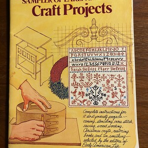 Puede incluir: Una portada de libro con fondo amarillo y el título "Sampler of Early American Craft Projects". La portada presenta ilustraciones de una mano trabajando en un proyecto de madera, un sampler con diseños de punto de cruz y un sampler con letras y números del alfabeto.