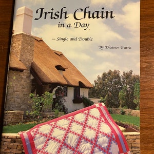 May include: A book titled "Irish Chain in a Day" by Eleanor Burns. The cover features a quilt with a red and white pattern, and a picture of a cottage with a thatched roof. The book is about quilting.