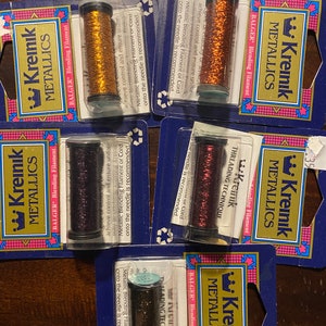May include: Five spools of Kreinik Metallic Blending Filament in various colors, including gold, copper, burgundy, and black. Each spool is labeled with the Kreinik logo and the words "BALGER Blending Filament".