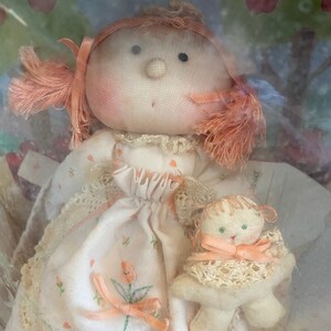 May include: A handmade doll with a white dress and a pink bow. The doll is holding a small white stuffed animal with a pink bow. The doll has a pink face and red hair.