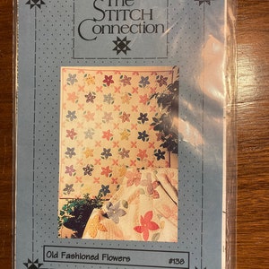 Pode incluir: Um padrão de colcha azul e branco com um design floral. O padrão é chamado de "Old Fashioned Flowers" e é numerado #138. O padrão é de The Stitch Connection.