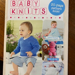 May include: A book cover for a knitting pattern book titled "Baby Knits". The cover features a blue knitted sweater, a pink knitted cat toy, a white knitted blanket, and a baby wearing a blue knitted sweater. The book includes 20 knitting patterns.