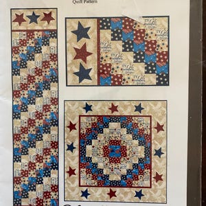 May include: A quilt pattern titled "Stars and Strips Sixes Table Set" with a patriotic theme. The design includes red, white, and blue stars and stripes. The set includes a table runner and two square quilt patterns, each measuring 35 inches by 35 inches.