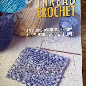 Pode incluir: Um livro intitulado "Ultimate Guide to Thread Crochet" com um quadrado de crochê azul na capa. A capa do livro também apresenta novelos de fio azul, branco e marrom.
