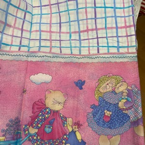 Può includere: Un tessuto vintage con un design stravagante. La parte superiore ha uno sfondo bianco con un motivo a griglia blu, viola e rosa. La sezione inferiore è rosa con personaggi di gatti dei cartoni animati.