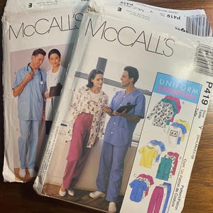 Peut inclure: Deux enveloppes de patrons de couture McCall's avec des images d'uniformes médicaux. L'une montre un homme et une femme en blouses bleues claires, l'autre une femme en veste fleurie et pantalon rose. Les patrons sont pour les essentiels de l'uniforme.